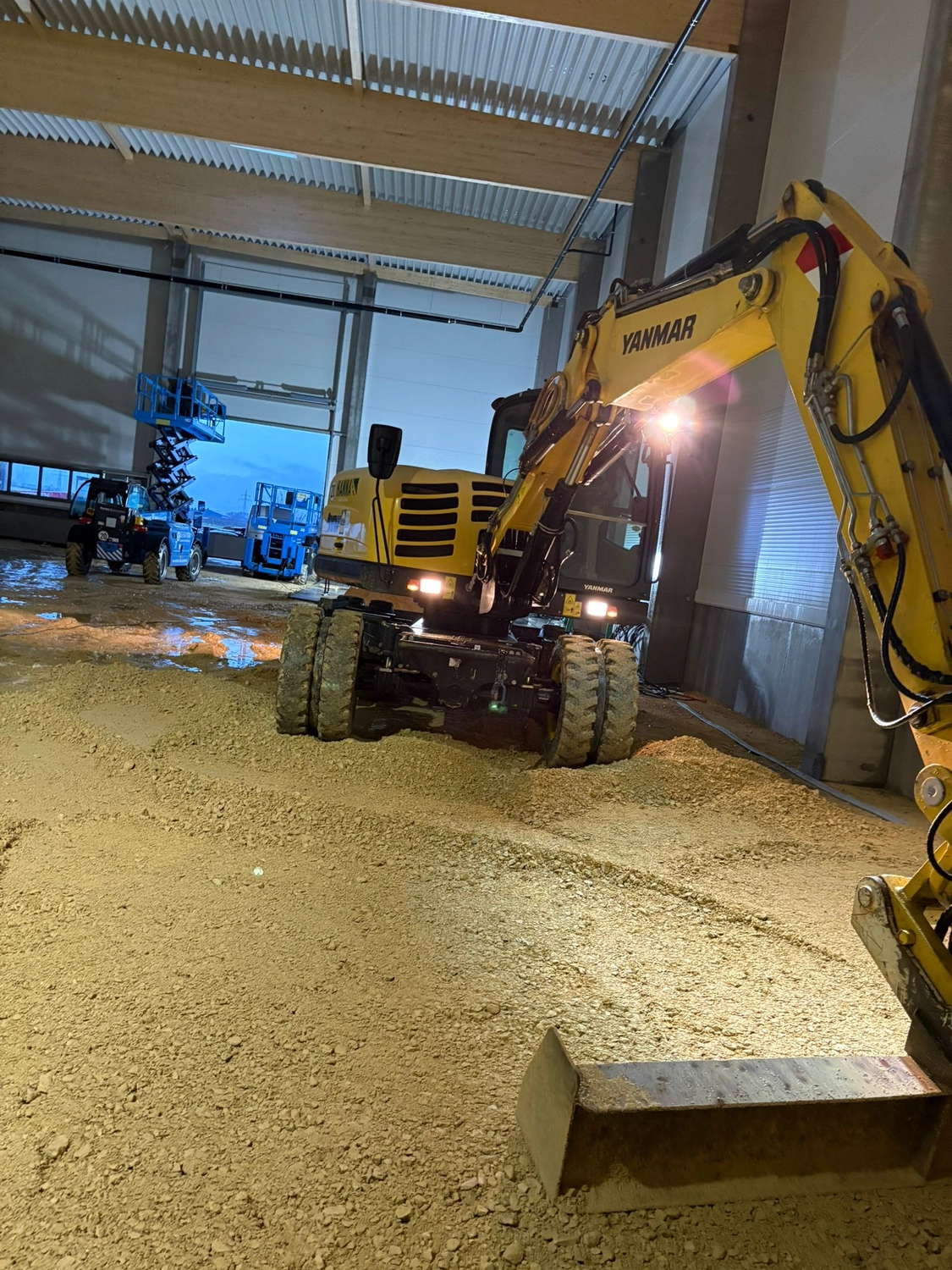 Gartenbau Brandenburg – Gartenarbeit – Das Bild zeigt einen Yanmar B95W Mobilbagger. Dieses Modell ist eine kompakte Maschine mit kurzem Heck, die für ihre Stabilität und Vielseitigkeit auf verschiedenen Baustellen bekannt ist.